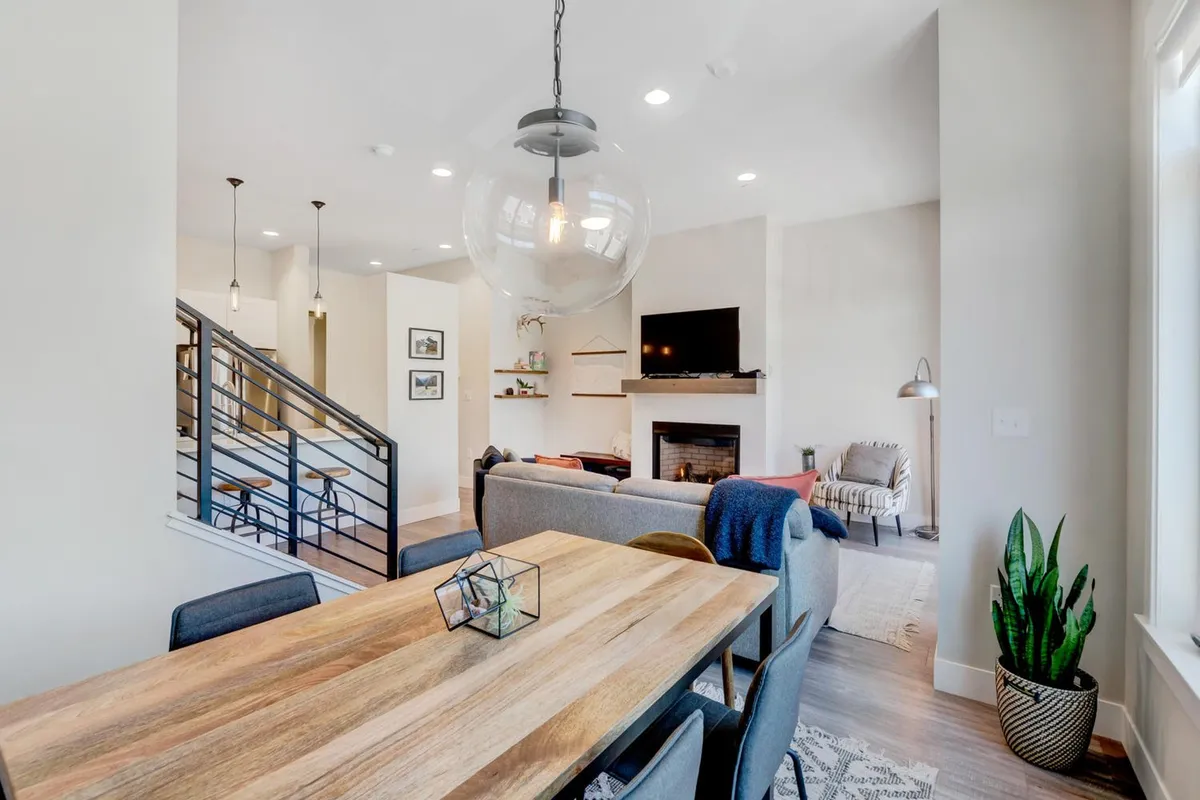 A spacious, inviting living area with a large dining table, elegant chandelier, modern fireplace, television, and comfortable sofa. The scene evokes a mood of togetherness, perfect for group dinners or relaxed evenings after exploring town.