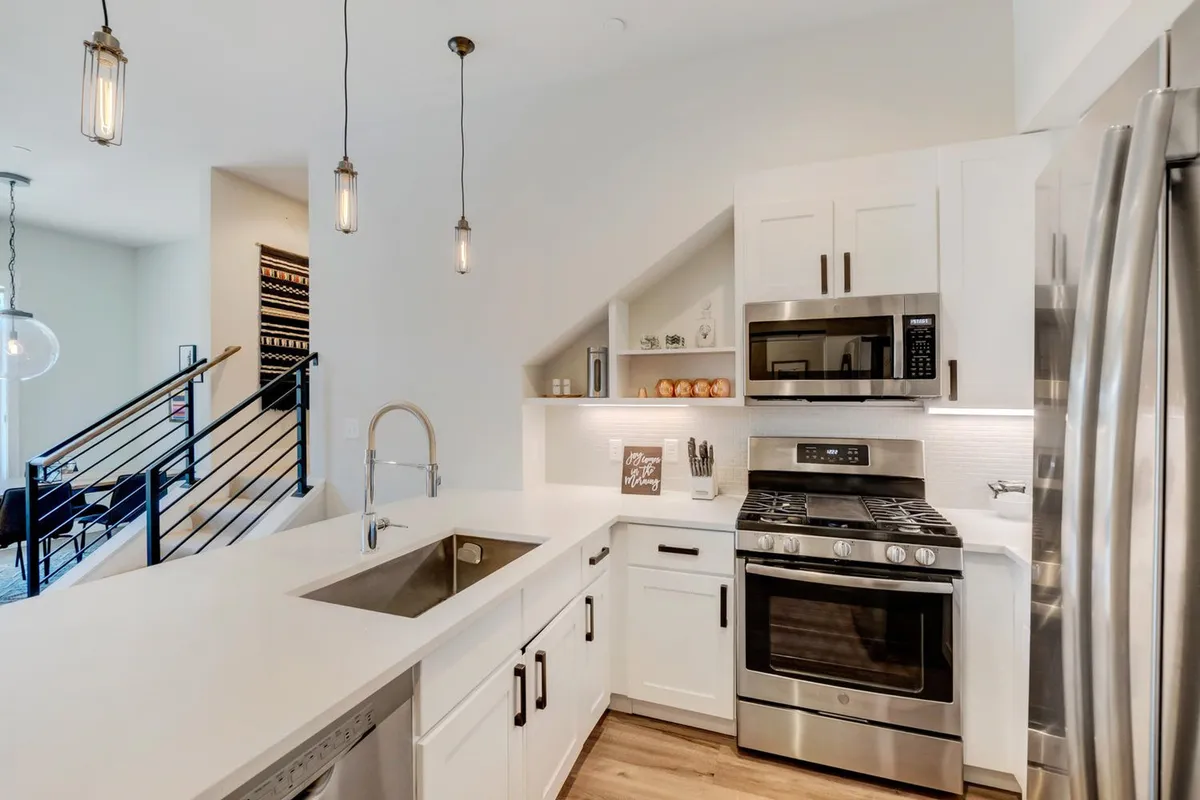 A modern chef’s kitchen with stainless steel appliances, white cabinetry, a pristine quartz countertop, and elegant pendant lighting overhead. The setup is both functional and stylish, suggesting a space where gourmet meals and entertaining are effortless.