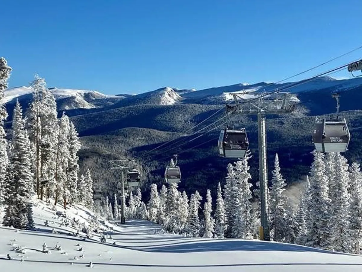 This dynamic exterior winter scene showcases ski lift gondolas gliding over snow-covered slopes, with a distant mountain range and evergreen trees providing a breathtaking Rockies backdrop. People are visible enjoying outdoor activities like skiing and snowboarding.