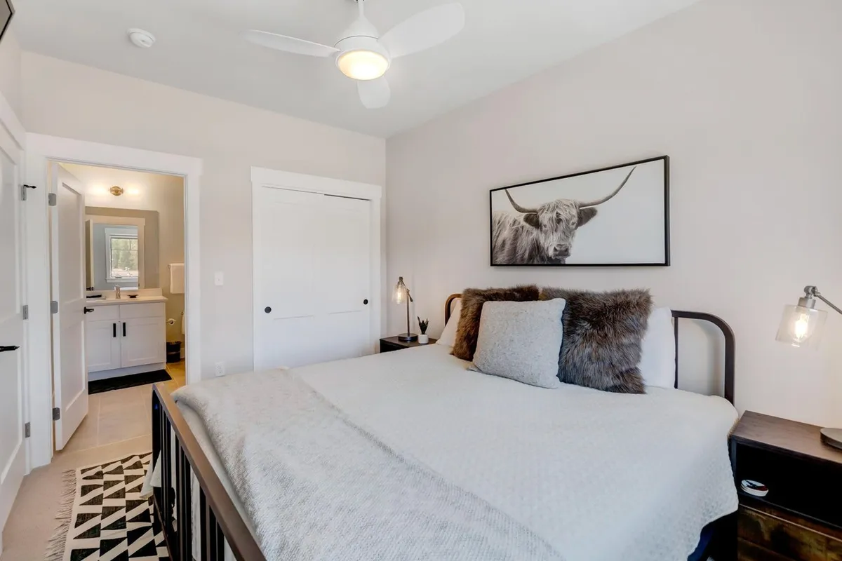 A cozy bedroom featuring a bed with textured bedding, a quirky piece of cow artwork, a nightstand, and stylish light fixtures. The inviting ambiance and practical layout fit well for families or groups seeking a welcoming space.