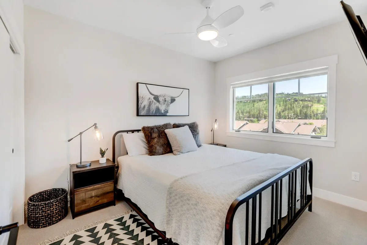 A serene bedroom with a plush bed dressed in premium bedding, tasteful artwork above the headboard, a nightstand with a lamp, and a window offering a calming view. The mood is tranquil and restful, perfect for relaxation after a day of mountain adventures.