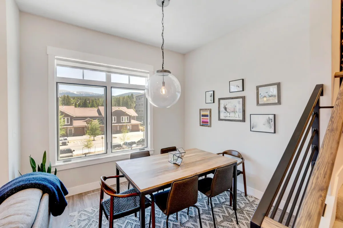 A bright dining area is pictured, with a large window offering scenic views, a dining table ready for meals or board games, and stylish decor. The space feels inviting and naturally connected to the outdoors.
