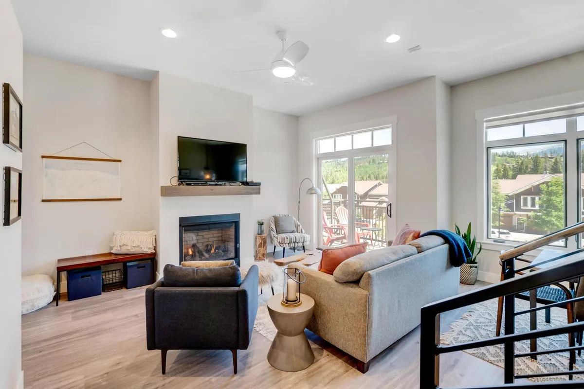 The image features a cozy seating area centered around a modern fireplace, with large windows letting in natural light and framing views of the outdoors. The arrangement invites relaxation and social interaction, ideal for movie nights or unwinding after a day out.
